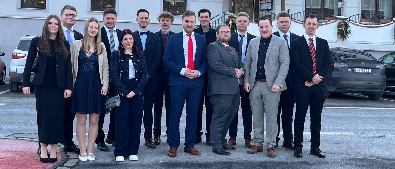 Eine Gruppe von Menschen in formeller Kleidung steht vor einem Gebäude. Sie posieren für ein Foto.