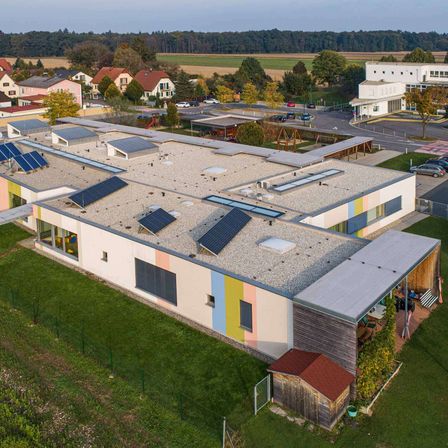 Luftaufnahme eines Schulgebäudes mit Solarmodulen auf dem Dach, umgeben von einem Rasenfeld und anderen Gebäuden.