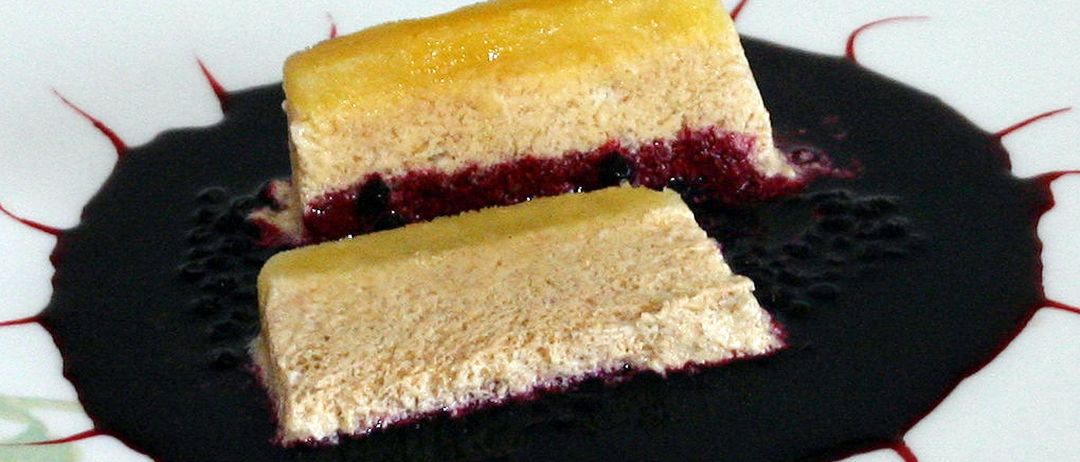 Zwei Stücke Käsekuchen mit einer Schicht Beerenkompott liegen auf einem weißen Teller mit schwarzer Beerensauce. Das Dessert ist mit roten Linien verziert.