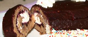 Ein Nahaufnahme eines Schokoladenkuchens mit einem aufgeschnittenen Stück, das eine cremige Füllung und eine Streusel von bunten Süßigkeiten auf der Oberseite zeigt.