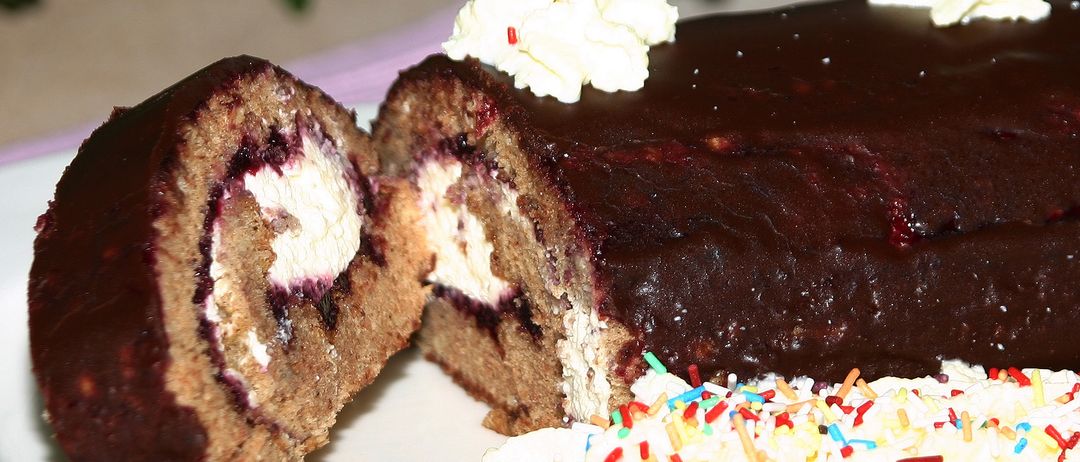 Ein Nahaufnahme eines Schokoladenkuchens mit einem aufgeschnittenen Stück, das eine cremige Füllung und eine Streusel von bunten Süßigkeiten auf der Oberseite zeigt.