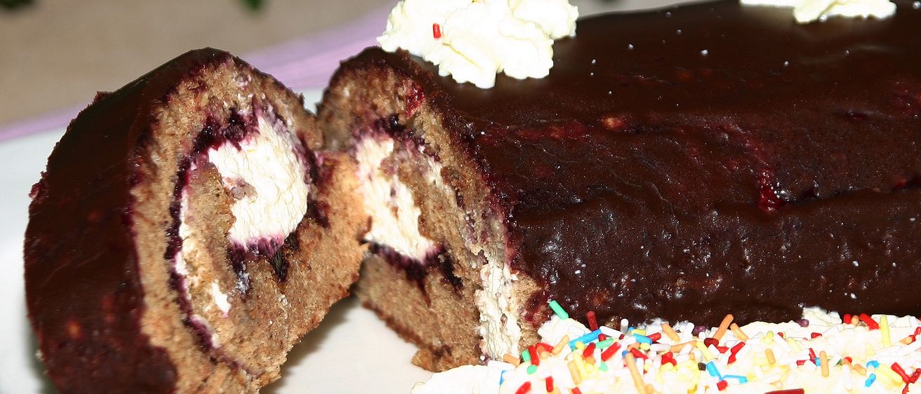 Ein Nahaufnahme eines Schokoladenkuchens mit einem aufgeschnittenen Stück, das eine cremige Füllung und eine Streusel von bunten Süßigkeiten auf der Oberseite zeigt.