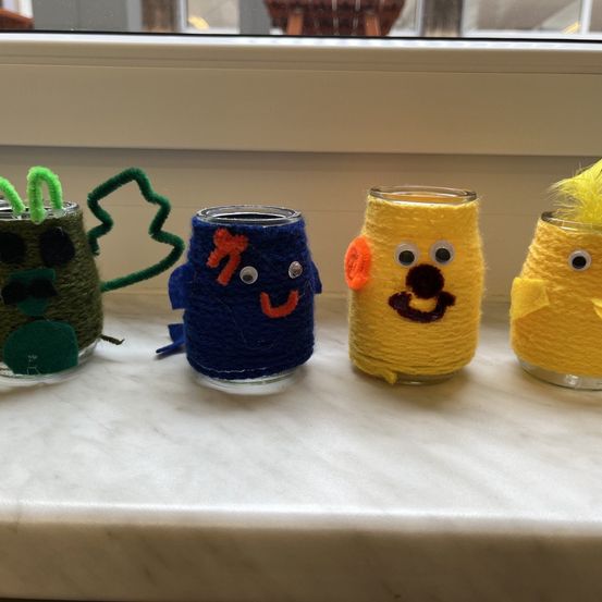 Vier Gläser mit Schnüren und Augen stehen auf einem weißen Tisch. Jedes Glas hat eine andere Farbe und Charakterdesign.
