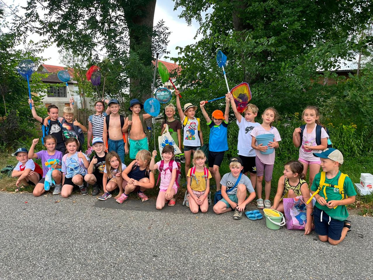 Eine Gruppe von Kindern, die draußen mit Fischernetzen posieren, einige knien oder stehen, und ein rotes Dach ist hinter ihnen sichtbar.