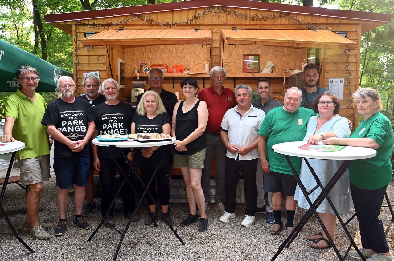 Eine Gruppe von Menschen in Freizeitkleidung posiert für ein Foto vor einer Holzstruktur mit einem Tisch voller Essen.