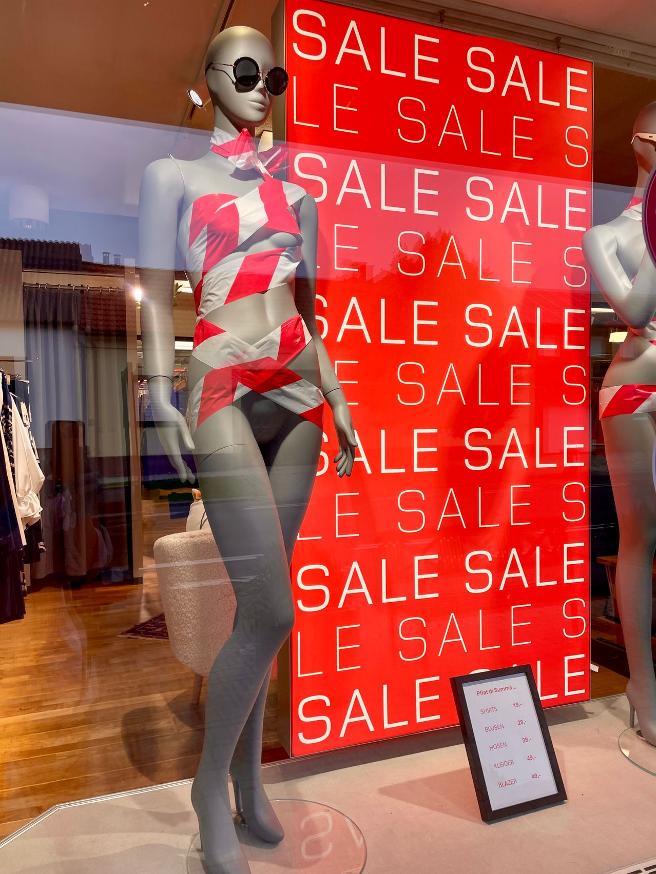 Eine Mannequin in einem roten und weißen Badeanzug steht vor einem roten SALE-Schild. Das Wort SALE ist in verschiedenen Positionen wiederholt.