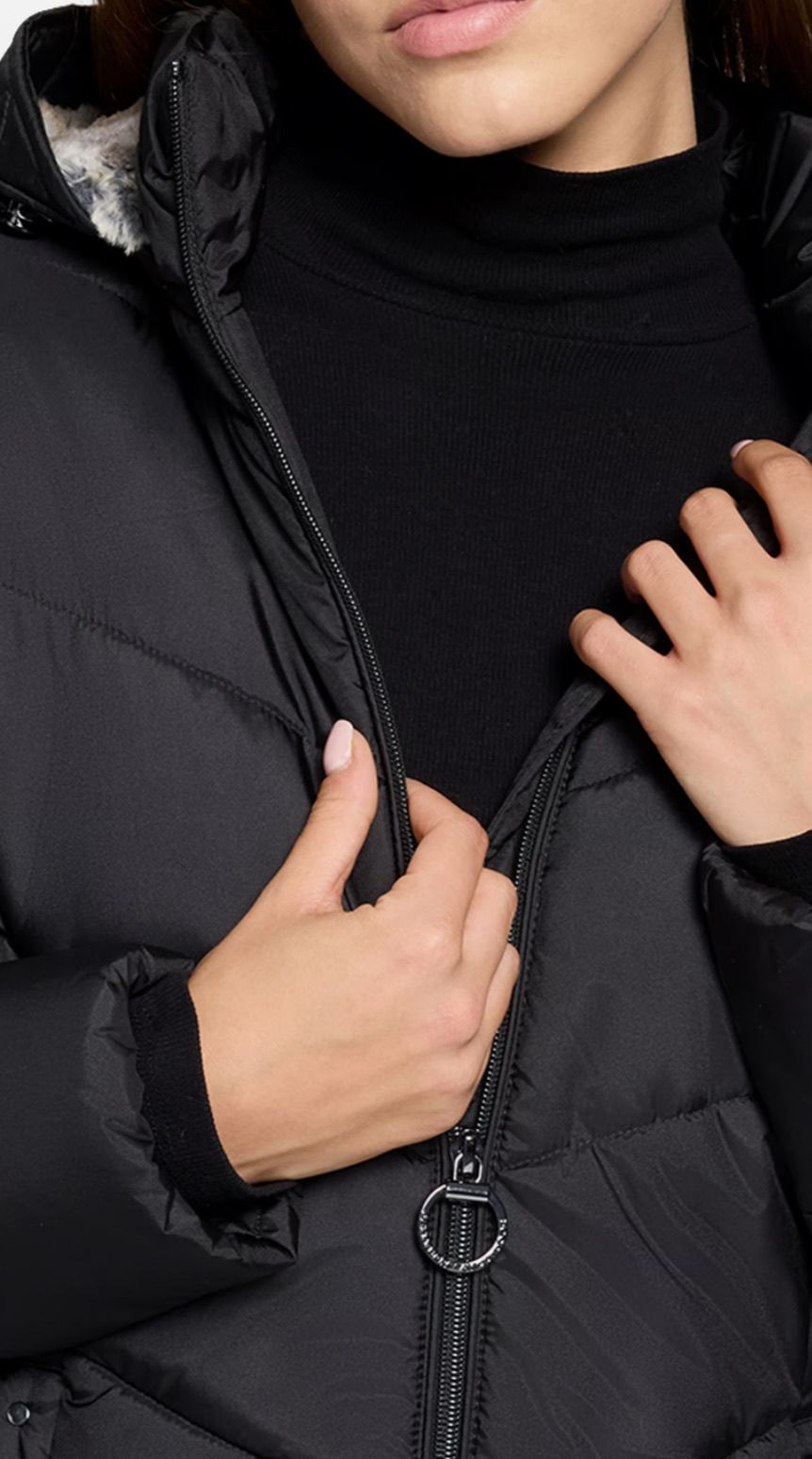 Eine Person trägt eine schwarze Daunenjacke mit Reißverschluss. Die Jacke ist hochgezogen und zeigt das schwarze Innenshirt.