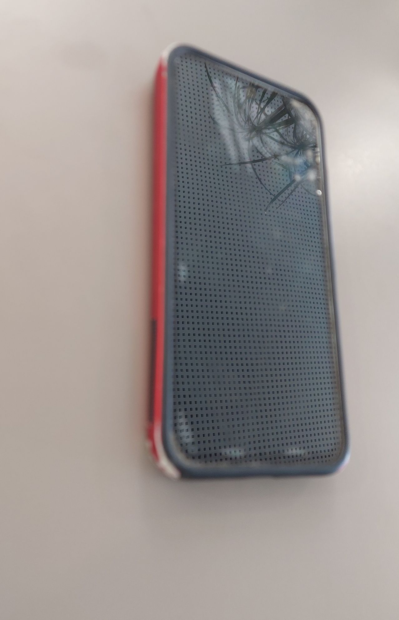 Ein rotes und graues Smartphone mit einem zerbrochenen Bildschirm und einem Spinnennetzmuster auf dem Glas.