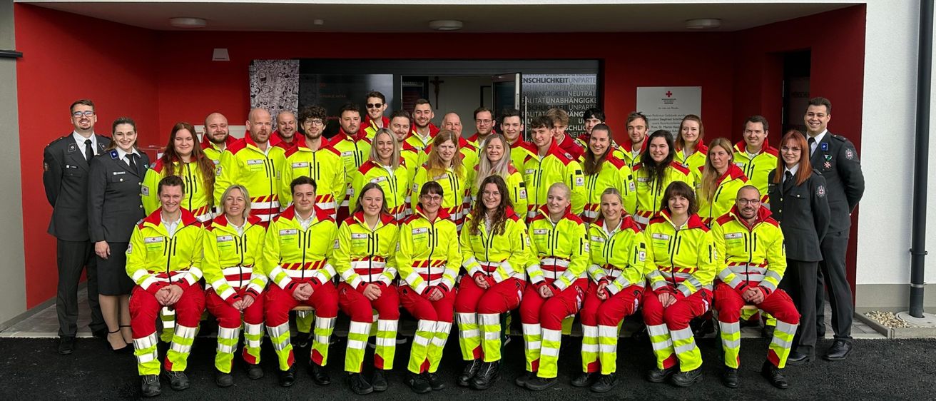 Eine Gruppe von Freiwilligen in leuchtend gelben Uniformen posiert für ein Foto vor dem Gebäude des Roten Kreuzes Steiermark.