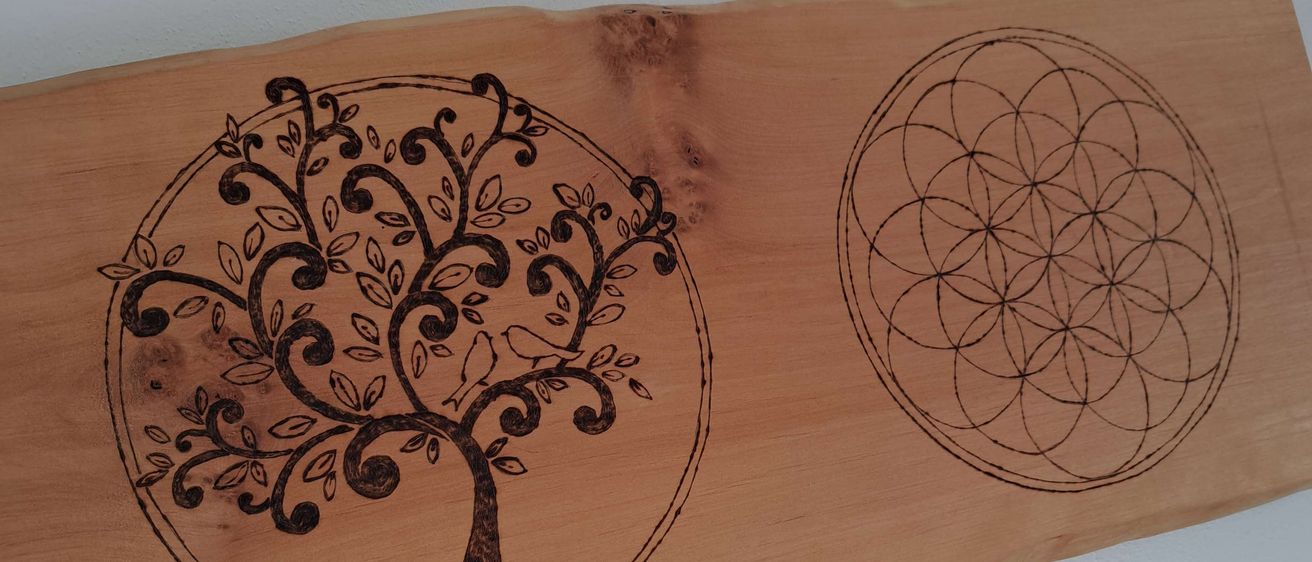 Ein Holzbrett mit zwei kreisförmigen Designs, eines zeigt einen Baum und das andere eine Lebensblume, beide fein geschnitzt.