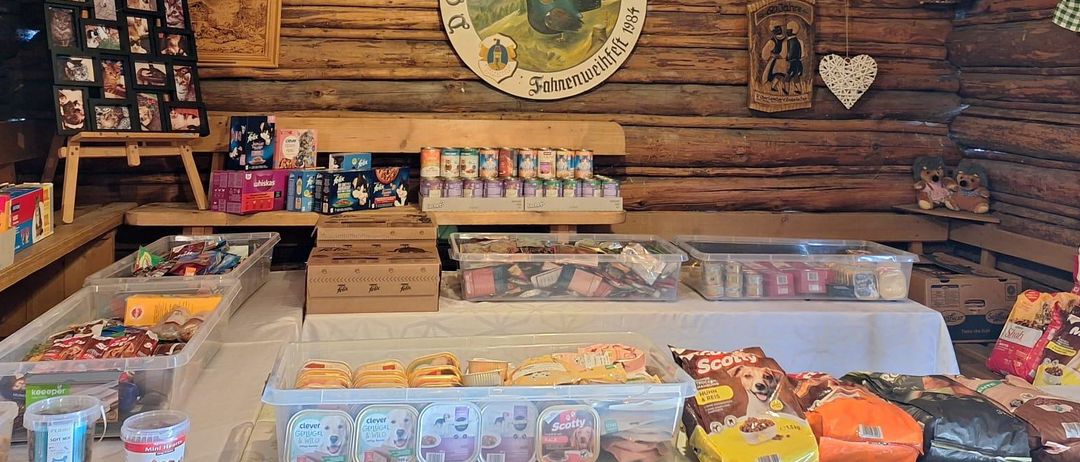 Ein Raum mit Holzwänden und Decke, einer Lampe und verschiedenen ausgestellten Artikeln. Mehrere Schachteln mit Snacks und Hundefutter stehen auf dem Tisch. Es gibt ein Schild an der Wand.