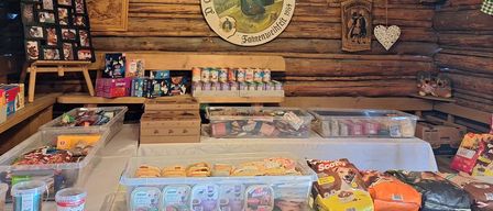 A room with wooden walls and a ceiling, a lamp, and various items on display. Several boxes of snacks and dog food are on the table. There is a sign on the wall.