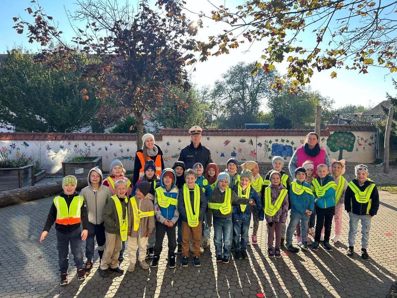 Eine Gruppe von Kindern und Erwachsenen in Warnwesten posiert sonnig im Park für ein Foto.