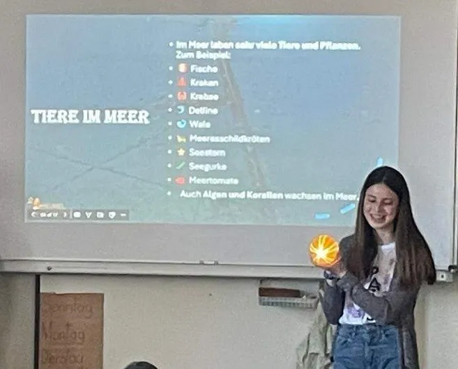 Eine Frau, die eine leuchtende Kugel hält, steht vor einer Projektionsleinwand mit einem Diagramm mit dem Titel Tiere im Meer. Sie lächelt.