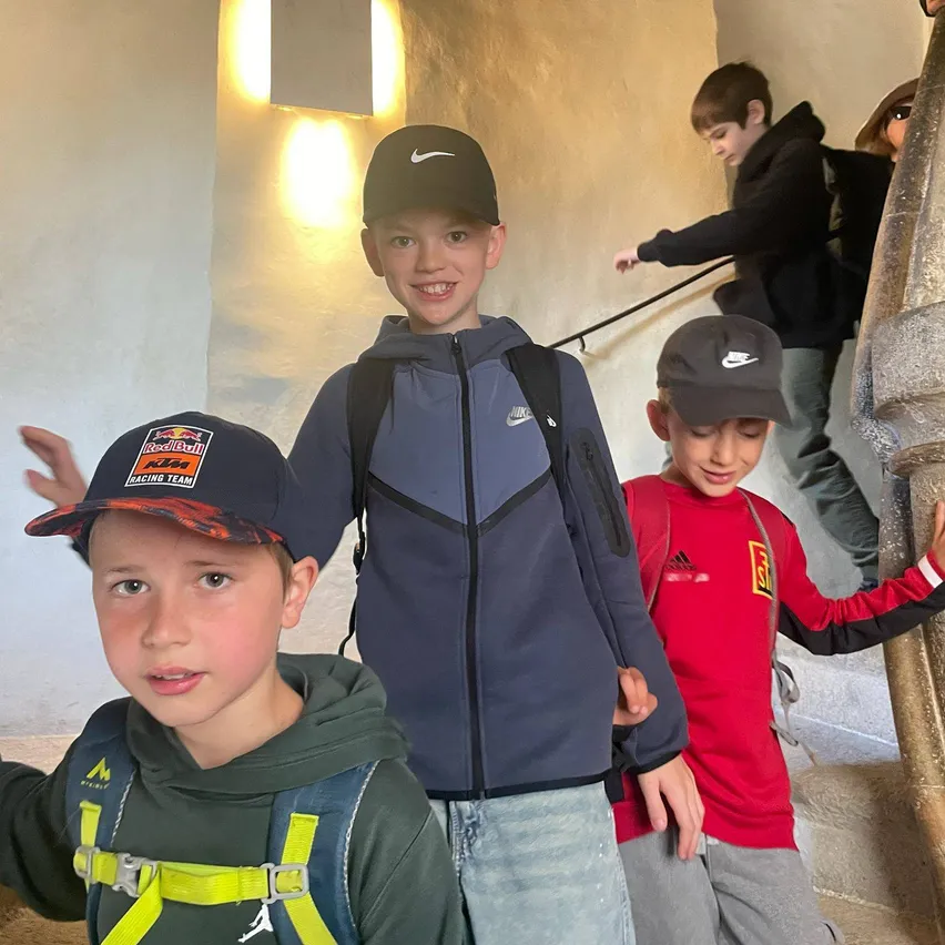 Drei Jungen posieren für ein Foto auf einer Treppe. Der Junge in der Mitte trägt eine blaue Jacke und eine Nike-Kappe. Der Junge links hat eine Kappe mit 'Red Bull Racing Team'. Der Junge rechts trägt ein rotes Shirt mit gelbem Logo.