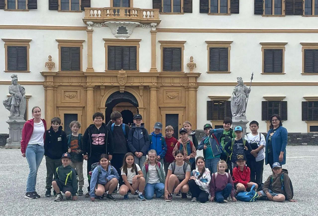 Eine Gruppe von Kindern und Teenagern posiert für ein Foto vor einem historischen Gebäude mit Statuen und aufwendigen architektonischen Details.
