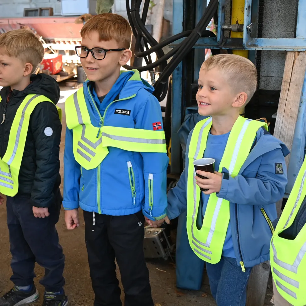Fünf junge Jungen tragen blaue Jacken und neongrüne Sicherheitswesten und stehen zusammen draußen.