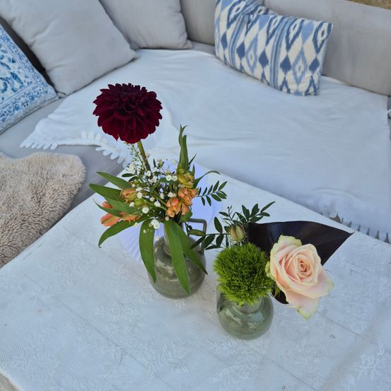 Eine Couch mit weißen Kissen und einem blauen Kissen mit Muster. Auf dem Tisch stehen drei Vasen mit Blumen.