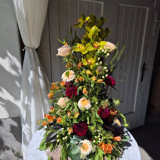 Ein farbenfrohes Blumenarrangement mit verschiedenen Farben wie Gelb, Orange, Weiß und Rot ist vor einer weißen Tür ausgestellt.