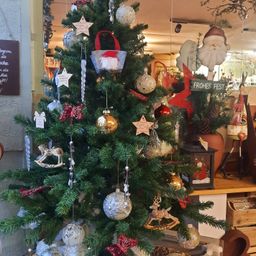 Ein mit Ornamenten und Dekorationen geschmückter Weihnachtsbaum, einschließlich einer Santa-Claus-Figur, hängt in einem Geschäft. Hinter dem Baum steht ein Holztresen mit verschiedenen Artikeln.