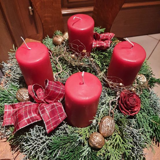 Ein Kranz mit vier roten Kerzen, rotem Band und einer roten Rose auf einem Holztisch.