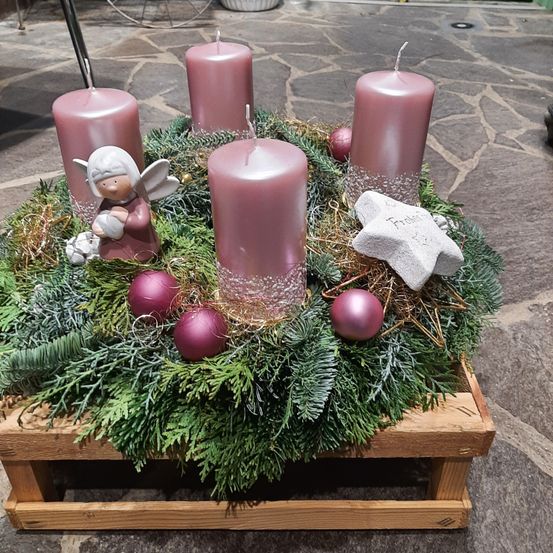 Ein Holzständer hält eine Adventskränze mit vier rosa Kerzen, einem weißen Stern und lila Ornamenten, auf einem Steinboden aufgestellt.