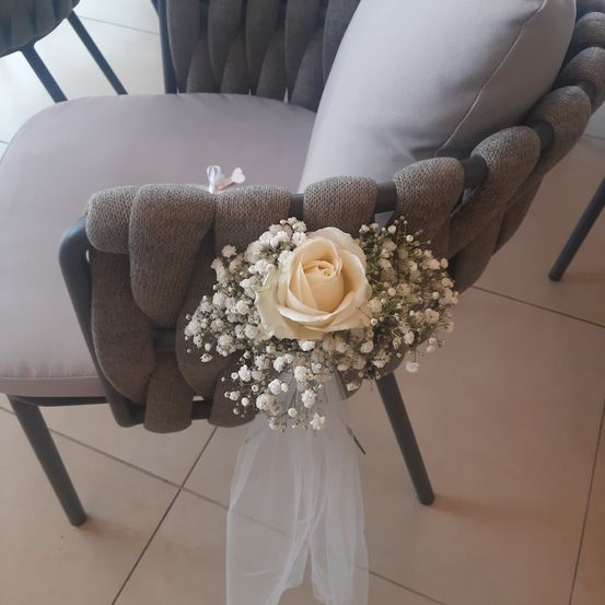 Ein Nahaufnahme einer einzelnen weißen Rose mit Babys Atem, gebunden an einen grau gepolsterten Stuhl mit gestrickten Riemen.