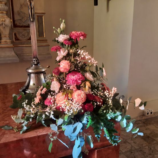 Eine Blumendekoration mit rosa und weißen Blumen steht auf einem Tisch. Dahinter befindet sich eine Statue und eine weiße Wand.