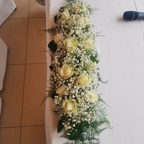 Eine elegante Blumenarrangement aus weißen Rosen und Babys Atmung schmückt einen Tisch, mit einem Mikrofon in der Nähe.