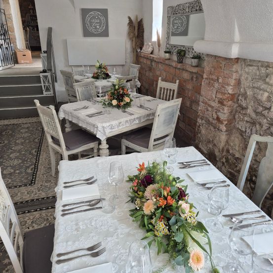 Ein eleganter Essbereich mit Tischen und Stühlen, Blumenarrangements und einer Ziegelwand. Der Raum hat einen Teppich, eine Treppe und einen gerahmten Spiegel.