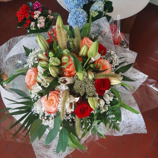 Ein Blumenstrauß mit verschiedenen Blumen, darunter rote, orange und weiße Rosen, weißes Babys atem und grüne Blätter.