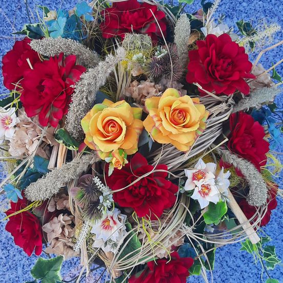 Eine lebendige Blumenzusammenstellung mit roten und gelben Rosen, verziert mit silbernen und blauen Elementen, präsentiert auf einer blauen Oberfläche.