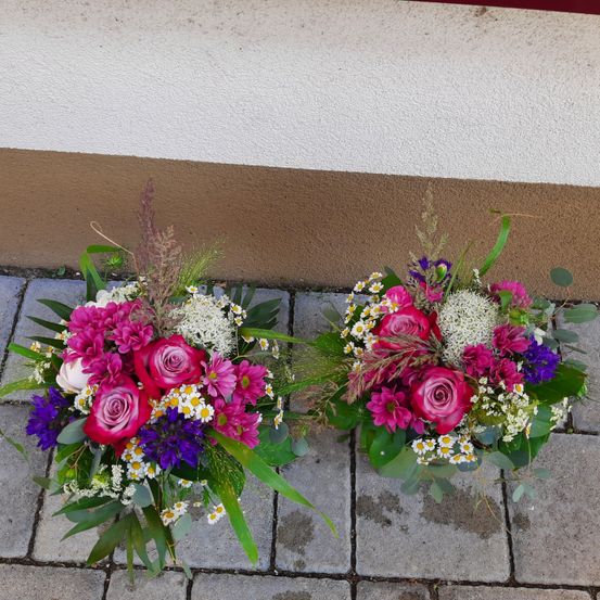 Zwei Blumenarrangements mit rosa Rosen, lila und weißen Blumen und grünen Blättern auf einem Ziegelboden.
