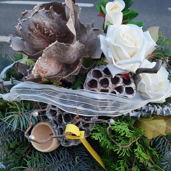 Ein Kranz mit weißen Rosen, braunen Blättern, Tannennadeln und gelben Bändern. Der Kranz besteht aus natürlichen Materialien.