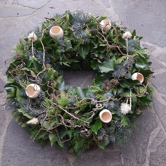 Ein Kranz aus grünen Blättern, Tannennadeln und kleinen Eierschalen liegt auf einer Steinoberfläche. Er hat eine kreisförmige Form mit Ästen und kleinen Zweigen.