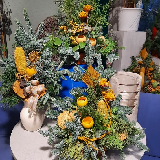 Drei dekorative Weihnachtskränze aus grüner Kiefer und gelben Blumen stehen auf einem Tisch. Jeder Kranz ist einzigartig mit unterschiedlichen Elementen.