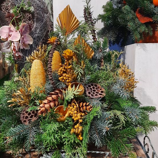 Eine dekorative Anordnung zeigt eine Mischung aus gelben und braunen Zapfen, grünem Laub und leuchtenden Blumen. Sie ist vor einem weißen Hintergrund mit einem Hauch von rosa Blumen und einem gelben Objekt in der Nähe.