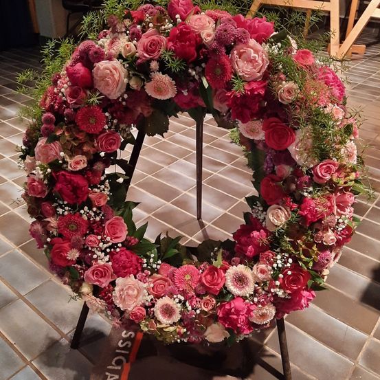 Ein kreisförmiger Blumenstrauß mit leuchtend roten und rosa Rosen, ergänzt durch weiße Babys Atem und Grün, steht auf einem gefliesten Boden.