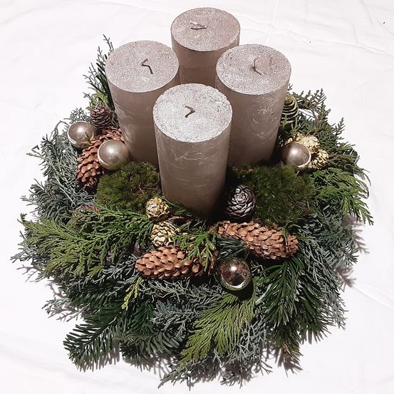 Ein Kranz mit vier Kerzen und Tannenzapfen. Der Kranz liegt auf einer weißen Oberfläche.
