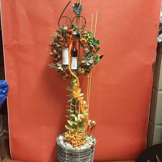 Eine dekorative Pflanzenarrangement mit zwei Flaschen Likör in einem Topf steht vor einem roten Hintergrund. Die Pflanze hat Beeren, grüne Blätter und eine Schleife, die darum gebunden ist.