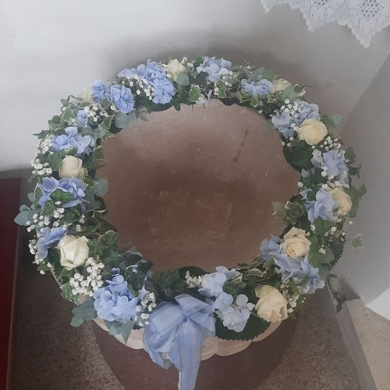 Ein kreisförmiger Kranz aus blauen und weißen Blumen mit Babysatem, der auf einem großen braunen Steinbecken mit weißem Rand ruht.