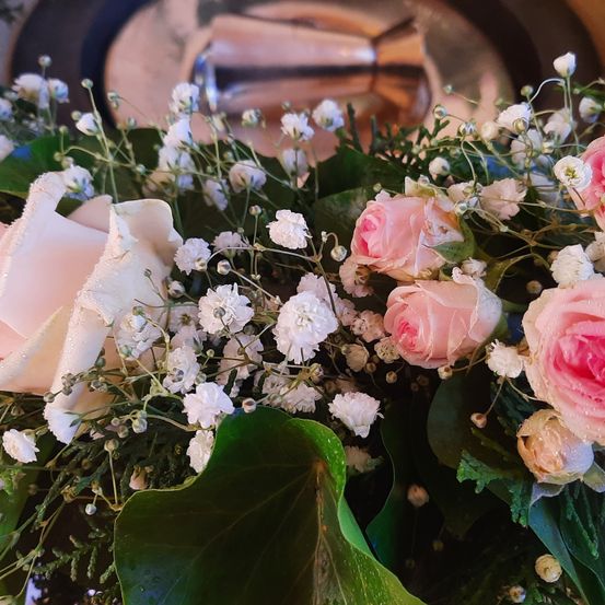 Eine Nahaufnahme einer Blumenarrangements mit rosa und weißen Rosen, Babys Atem und grünen Blättern. Die Blumen sind in einem Strauß arrangiert.
