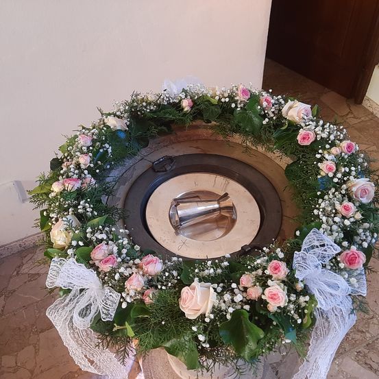 Ein Taufbecken, geschmückt mit einem runden Kranz aus rosa und weißen Rosen und Grün, steht auf einem gefliesten Boden in einer Kapelle.