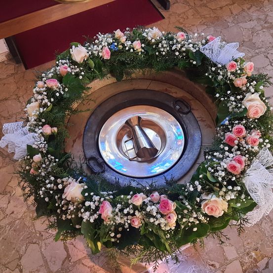 Ein Blumenkranz umgibt ein Taufbecken, geschmückt mit weißen, rosa und Babys Atem Blumen, mit einem silbernen Becken in der Mitte.
