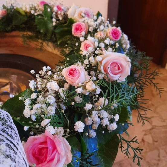 Eine kreisförmige Anordnung von rosa und weißen Rosen und Babys Atem mit grünen Blättern und einer blauen Vase auf einem gefliesten Boden.