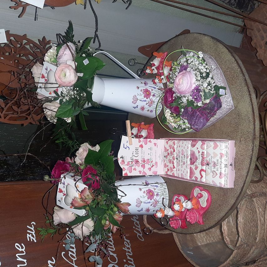 A display of various flower arrangements and gifts, including floral bouquets in vases and heart-shaped boxes, placed on a table with decorative elements.