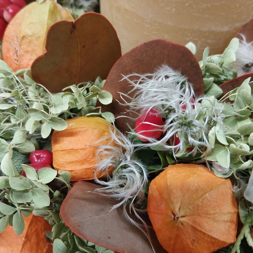Ein Nahaufnahme einer bunten Herbstgirlande mit getrockneten Blättern, kleinen Kürbissen und roten Beeren.