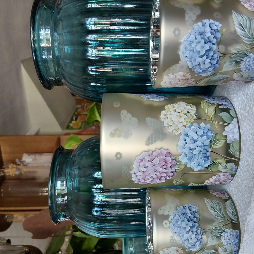 Three teal glass vases with gold floral designs and butterflies are stacked. The vases have a shiny finish, and the flowers are in shades of blue and pink.