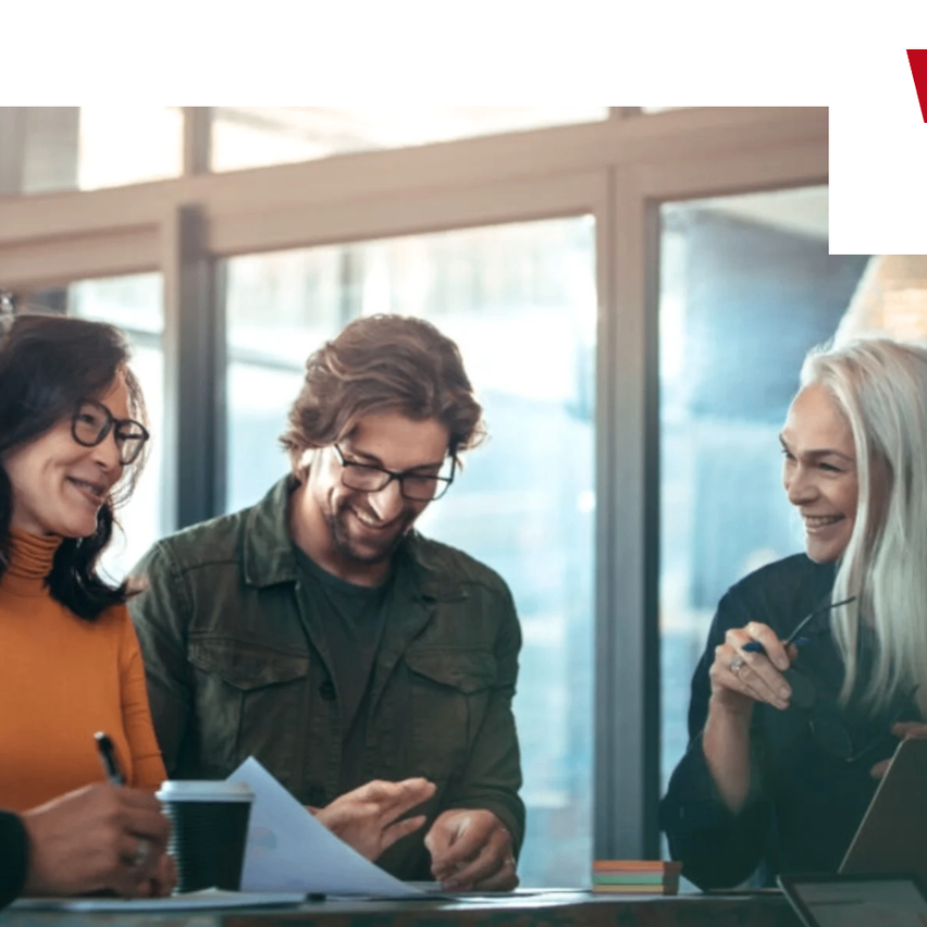 Vier Menschen sitzen lächelnd um einen Tisch herum und diskutieren. Zwei Frauen und zwei Männer, einer hält einen Stift und Papier, der andere einen Laptop.