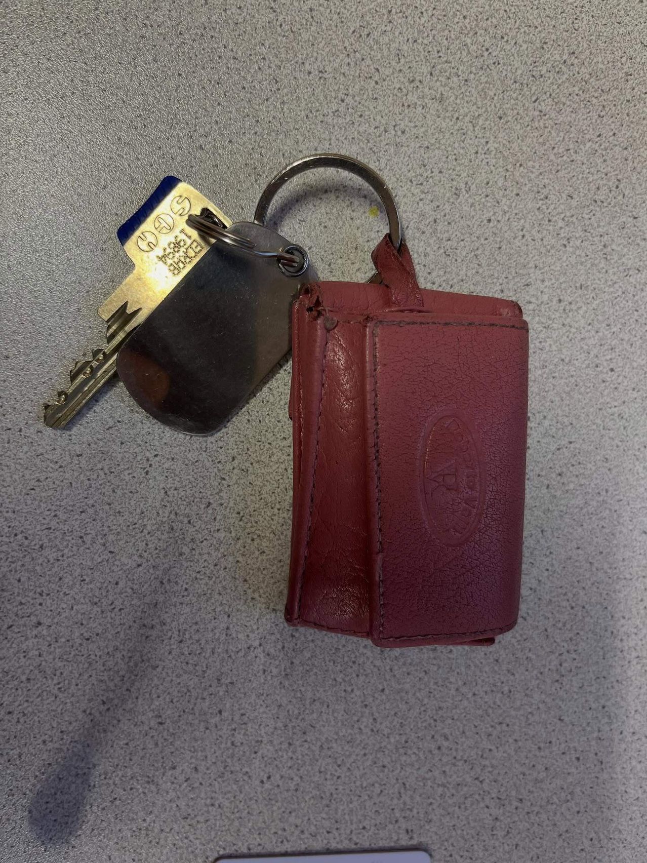 Ein Paar Schlüssel mit Schlüsselbund und einer roten Lederbrieftasche auf einer grauen Oberfläche.